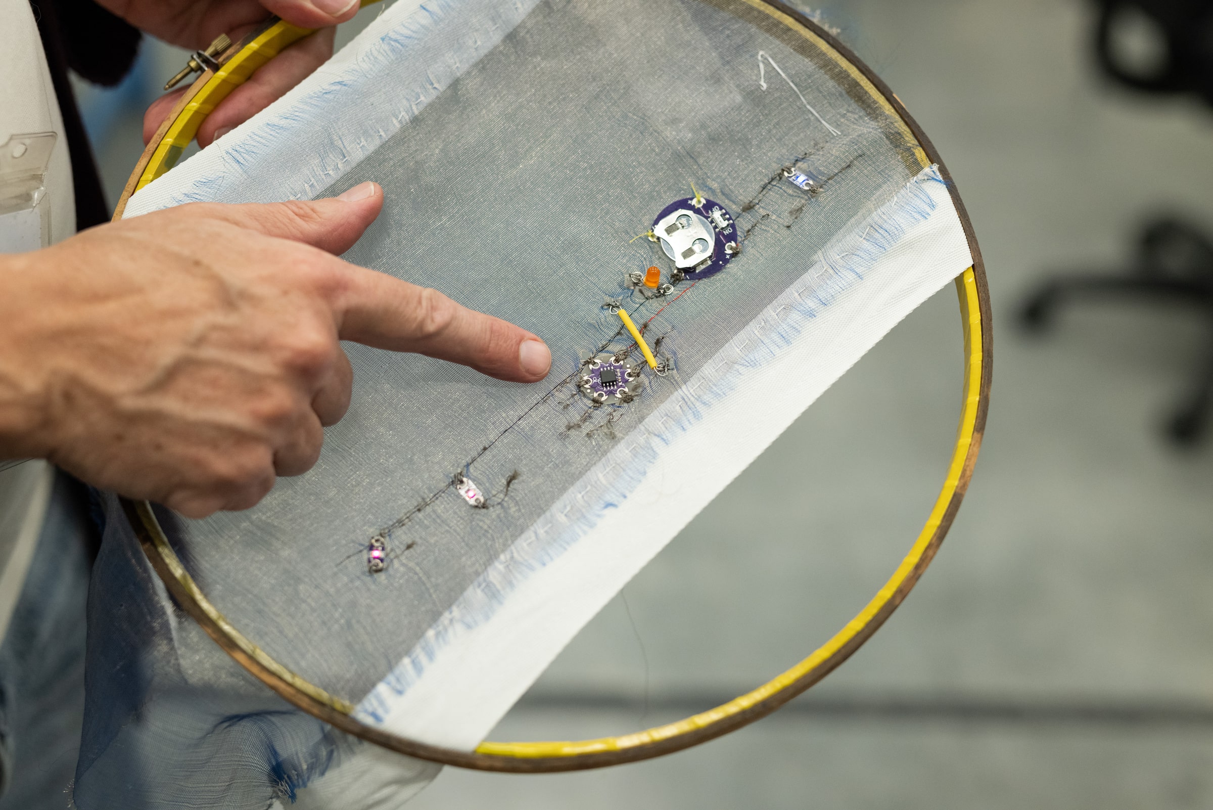Loop with stretched fabric containing an embroidered circuit, a finger points to the circuit.