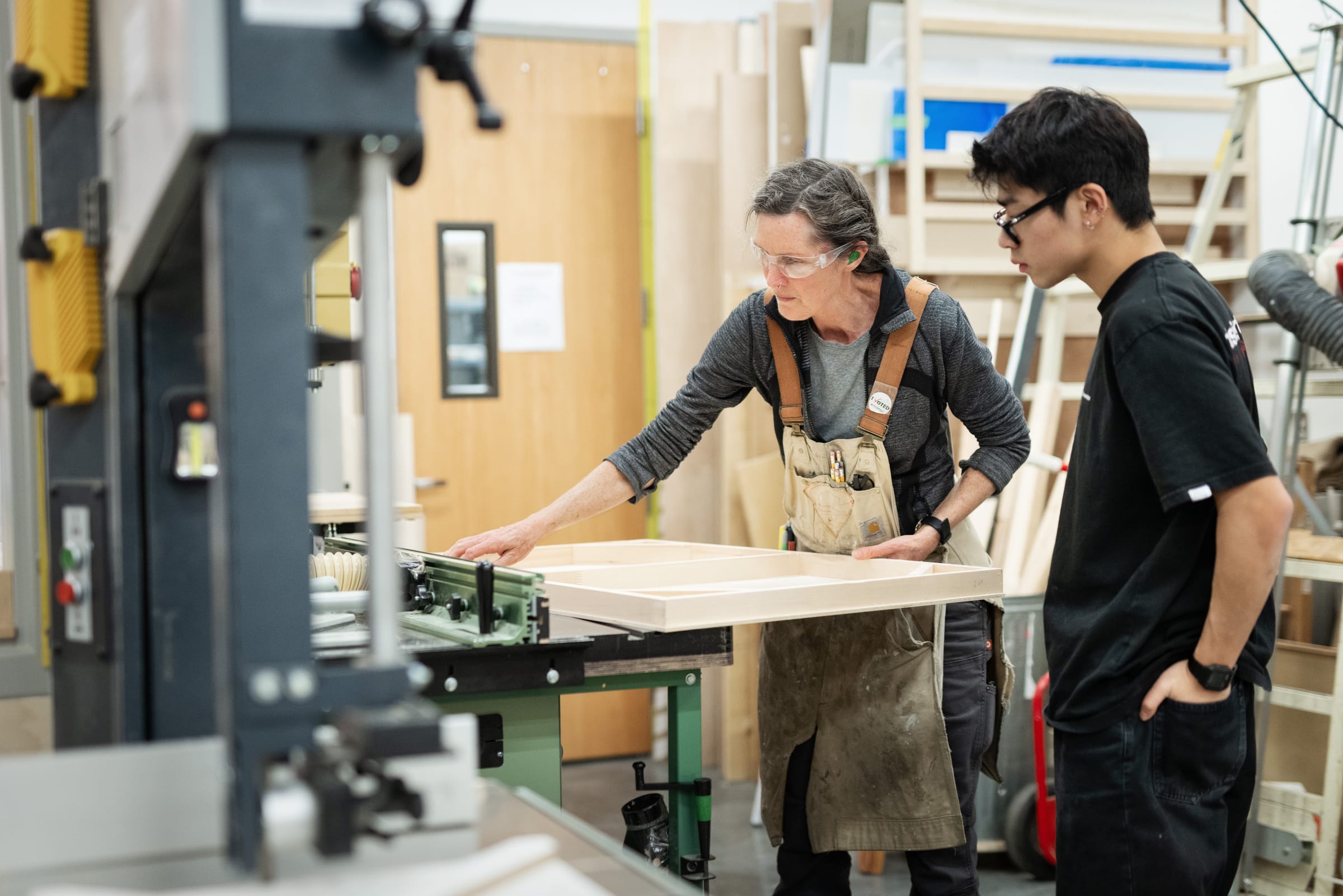 Technician cutting a panel board with a student in the wood shop.