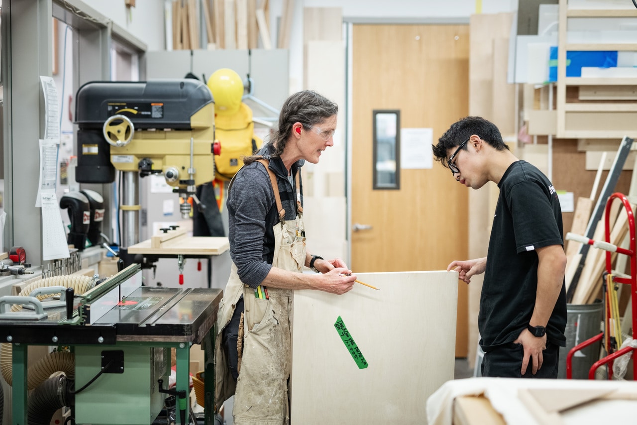 Technician helping a student measure a panel board in the wood shop.