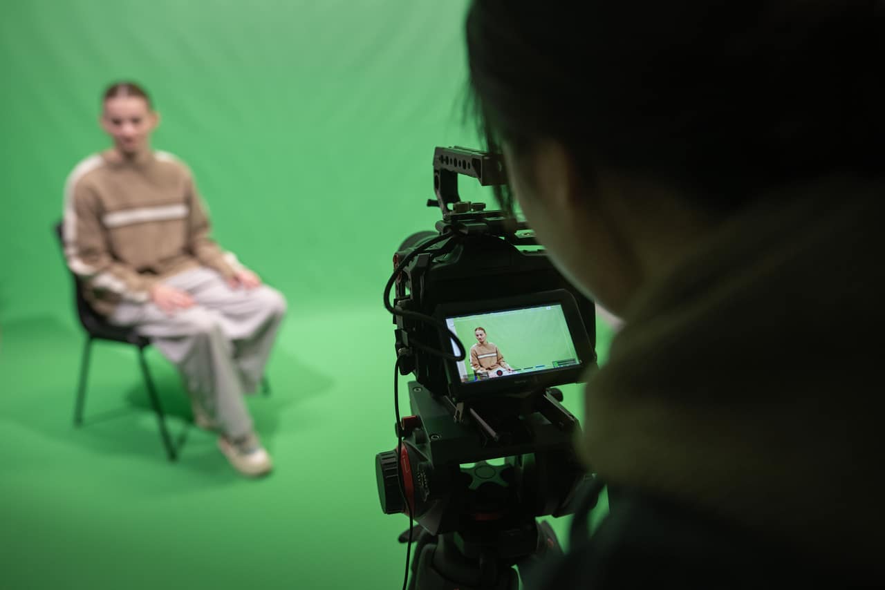 Student photographing a sitting subject in front of a green screen.