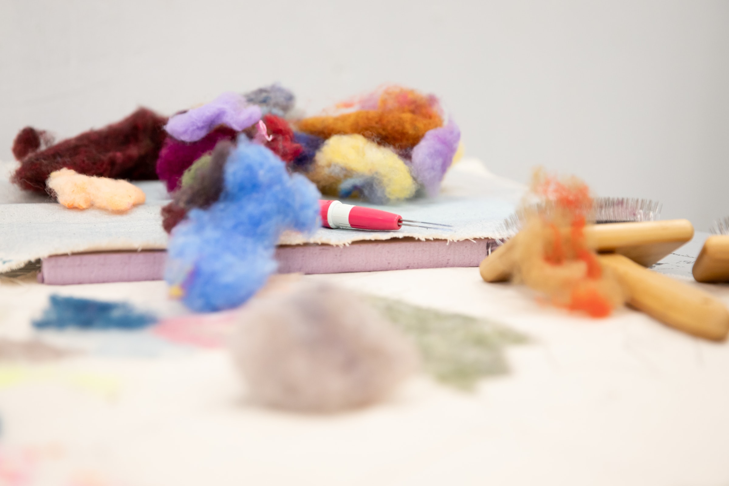 Close-up of colorful wool tufts, felting tools, and brushes spread across a workspace.