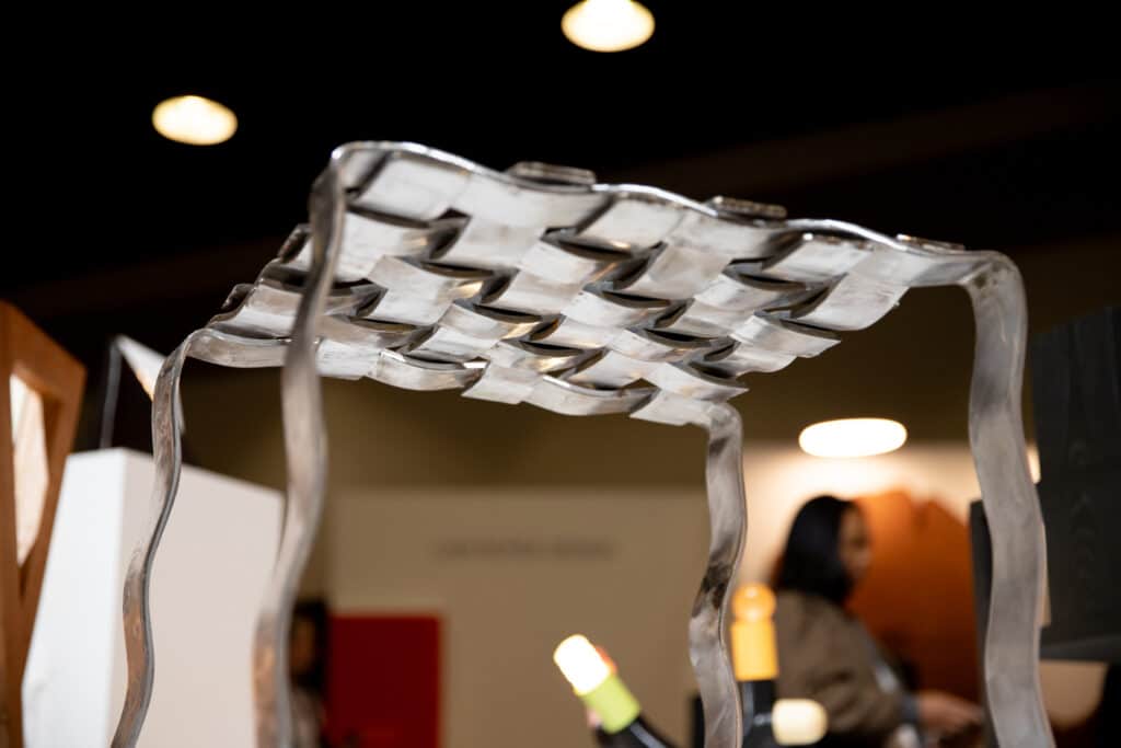 A close-up of a woven metal table with curved legs, shown from underneath.