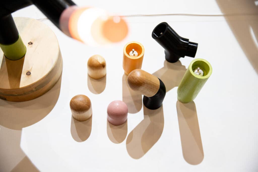 Assorted colourful wooden and painted lamp components, including bulb holders and bases, arranged on a white surface.