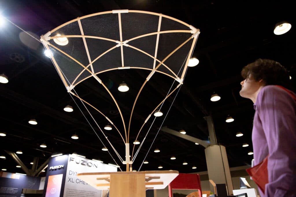 	A person looking up at a large wooden and fabric structure shaped like an open canopy, displayed indoors.