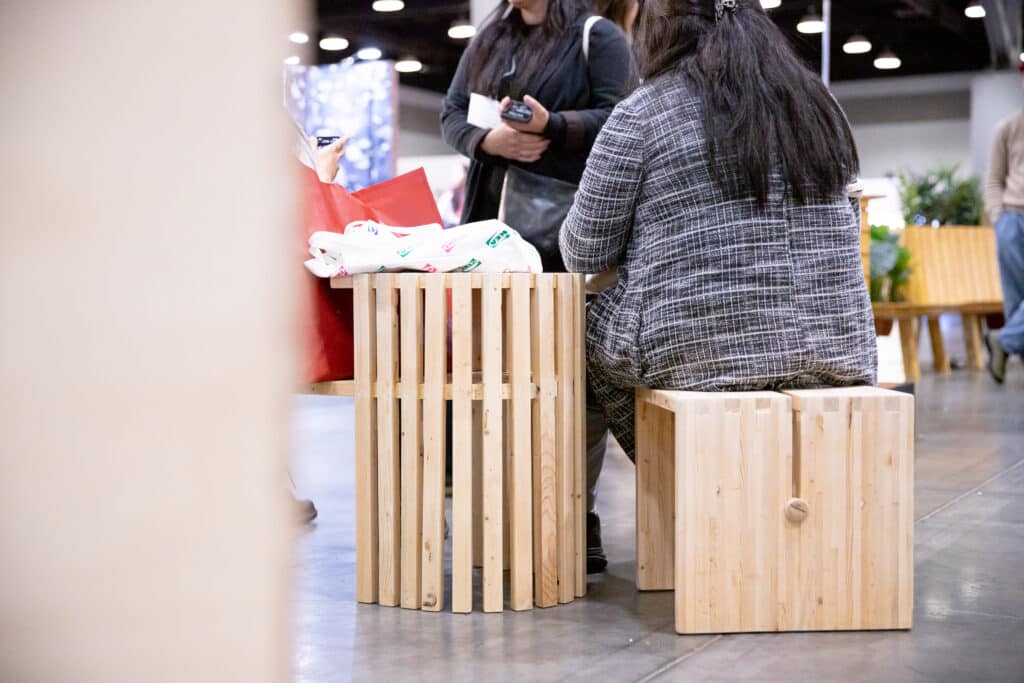 Close-up of two people seated on wooden stools with slatted sides at the trade show.