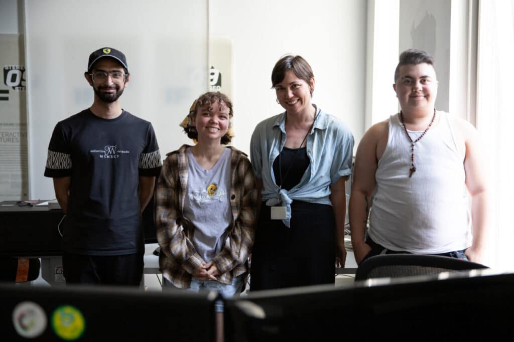 Four people standing together in a bright room, smiling at the camera.
