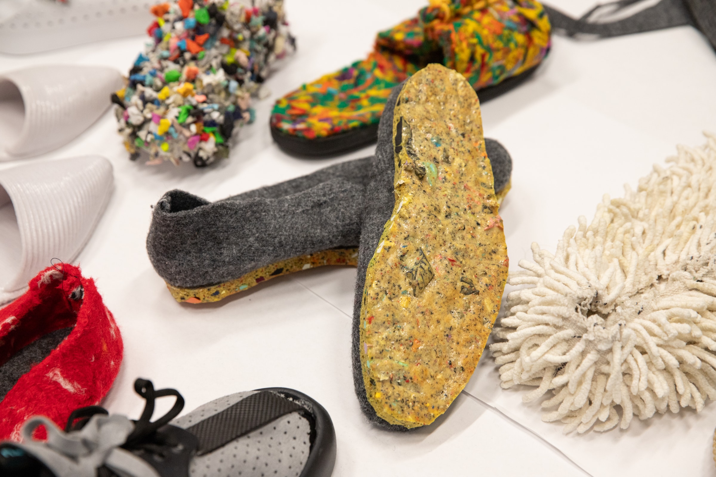 Several pairs of modified shoes displayed on a table. Textures include white spikes, colourful nodules, and colourful soles.