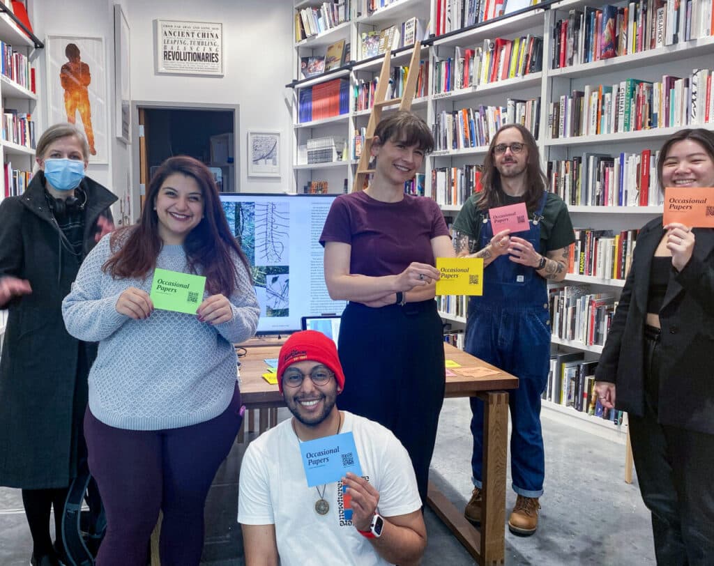 Group of six people in a bookshop, smiling and holding brightly coloured pamphlets titled Occasional Papers.