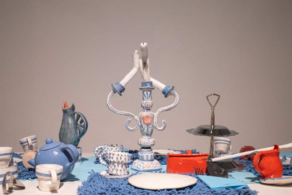 A thoughtfully arranged table setting with ceramic objects, a hospital blanket, metal elements, and found materials.