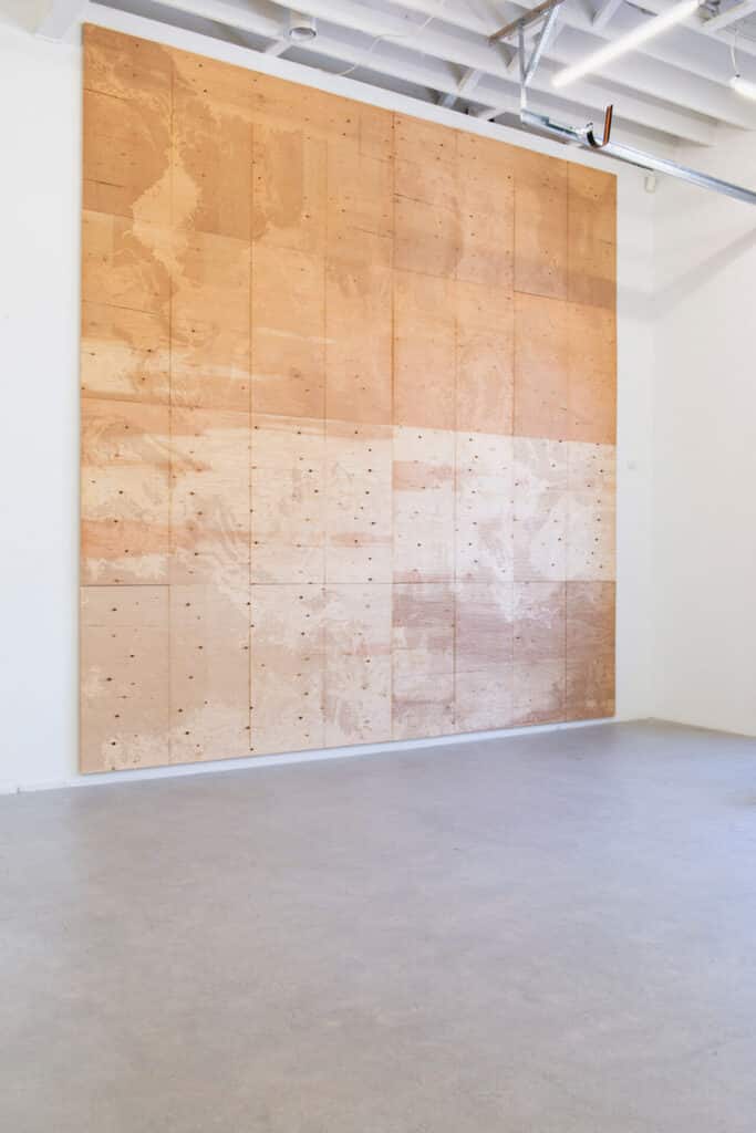 A large gallery wall covered with light and dark wooden panels arranged in a grid pattern, showing visible grain and markings
