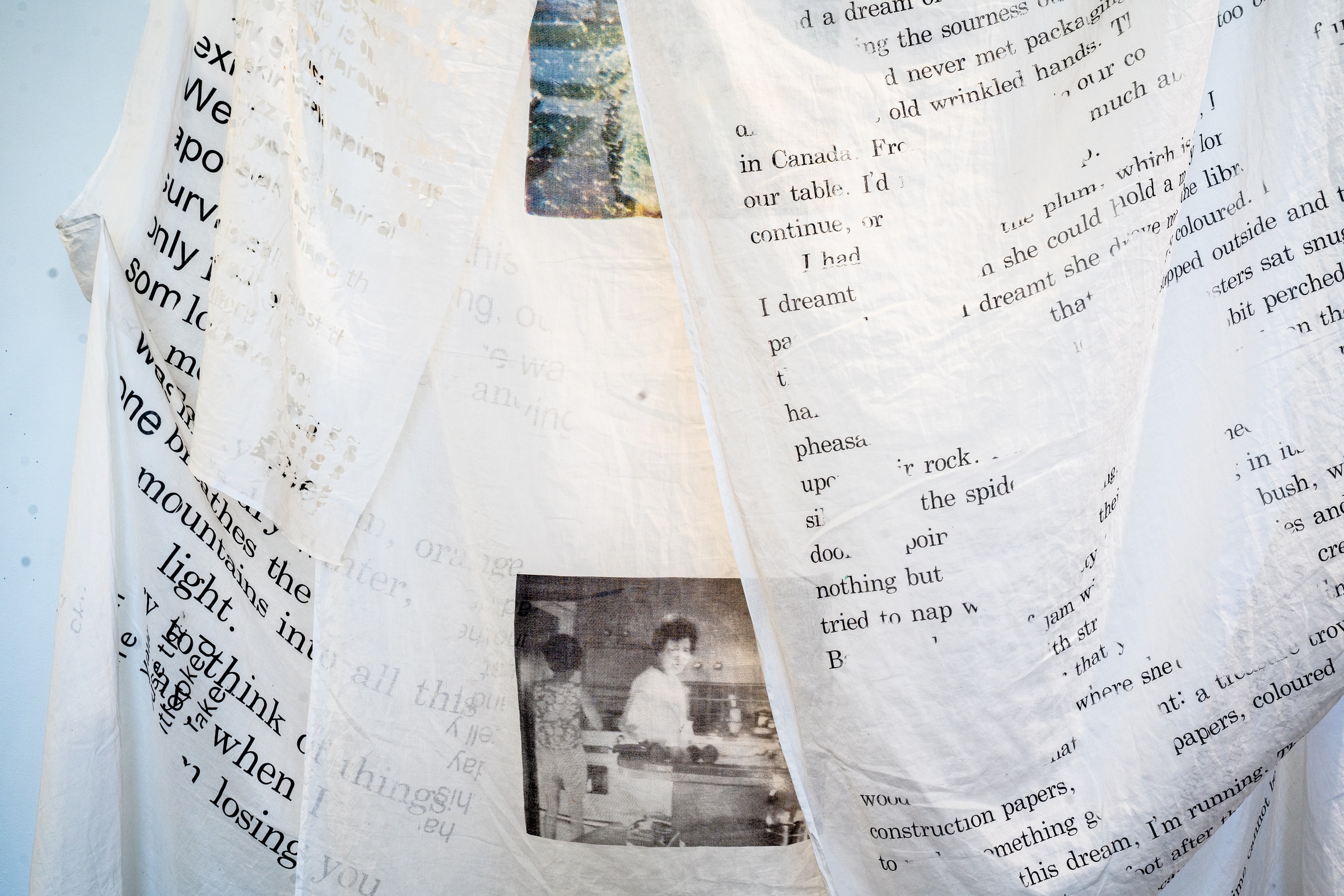 Close-up of a fabric artwork printed with text and a black-and-white photograph of two people in a kitchen.