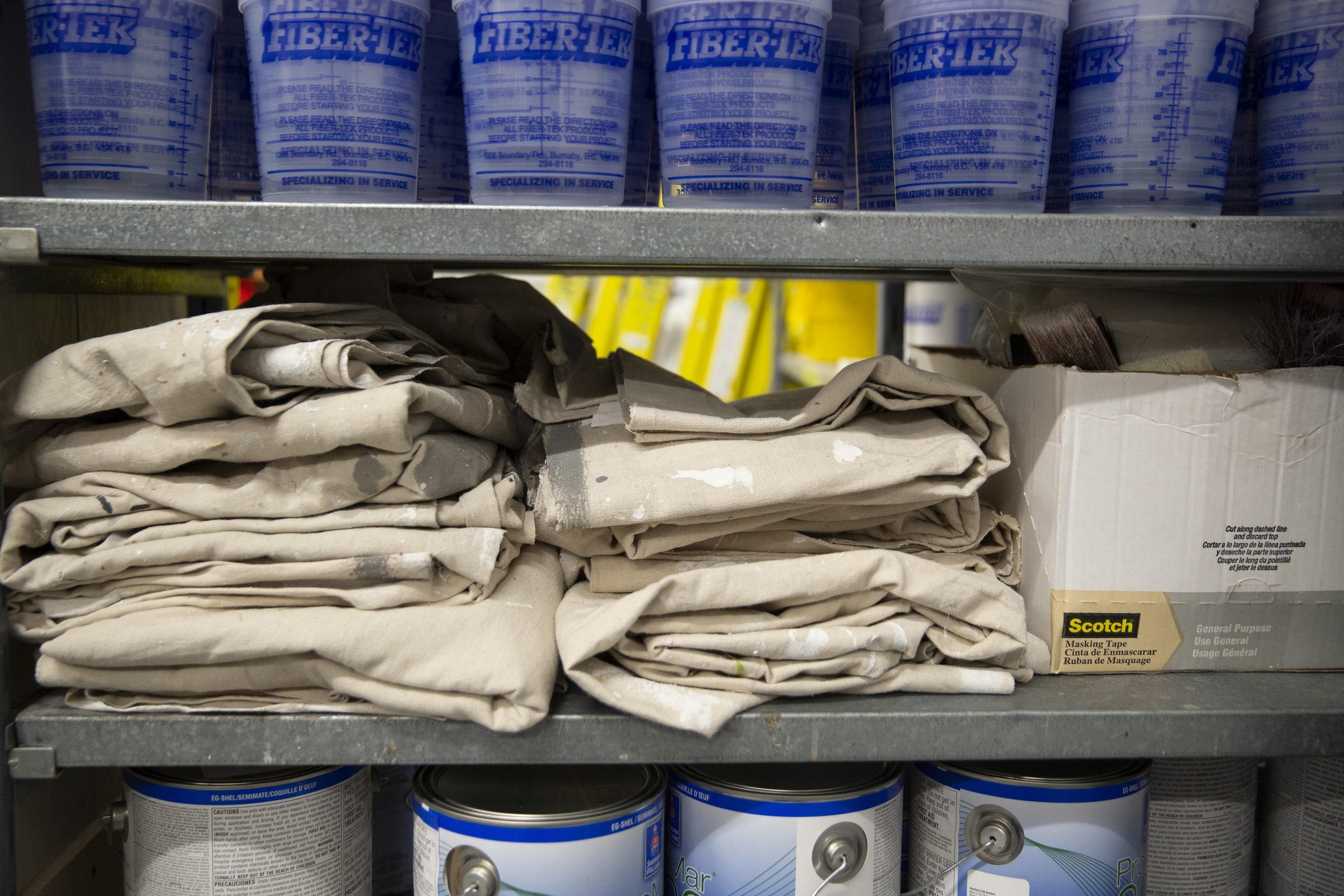 Paint tubs, white canvas and cans full of white paint stacked on metal shelving.