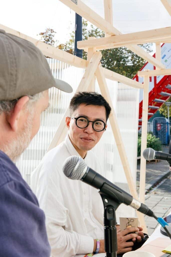 Close-up of two people talking into microphones during a discussion inside a wooden pavilion.