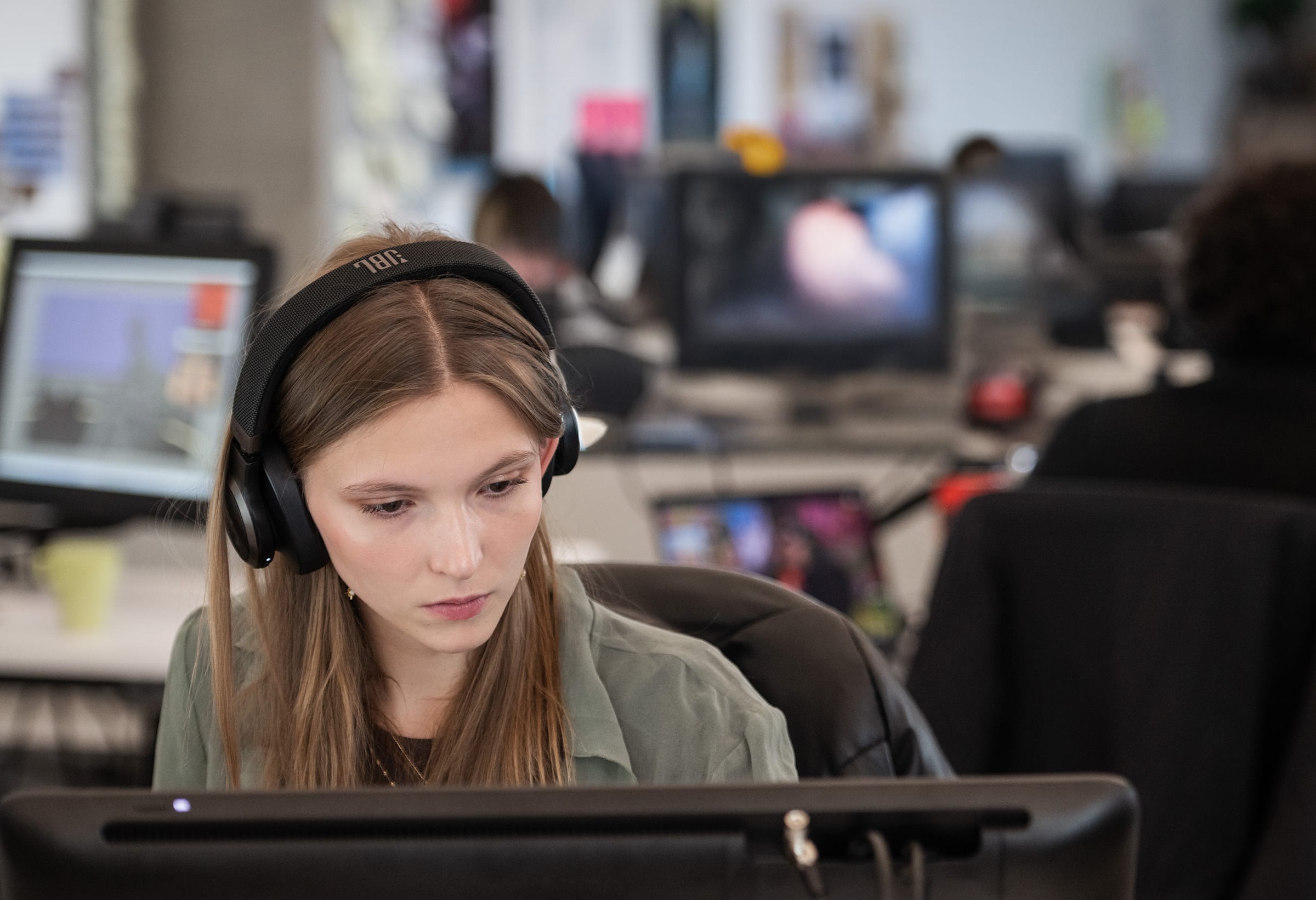 Student wearing headphones and working at a computer in a busy design studio environment.
