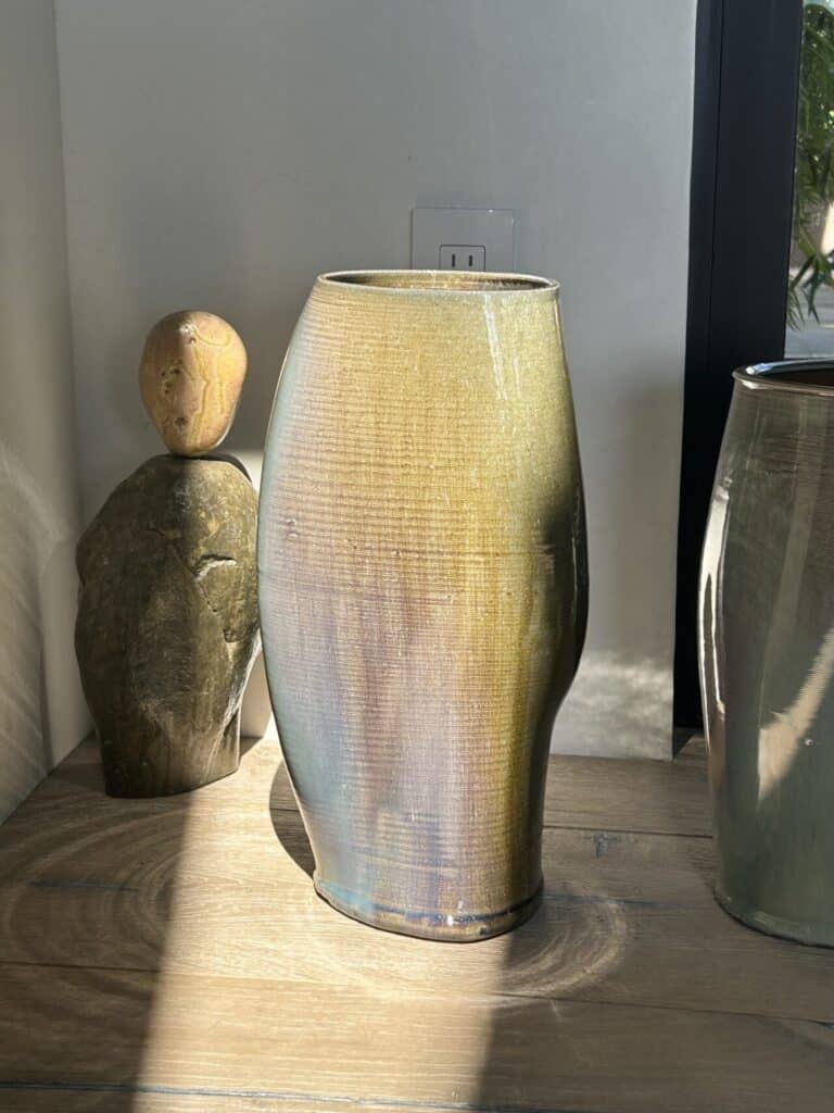 Large ceramic vase with a glossy yellow-brown glaze sitting on a wooden surface in sunlight.