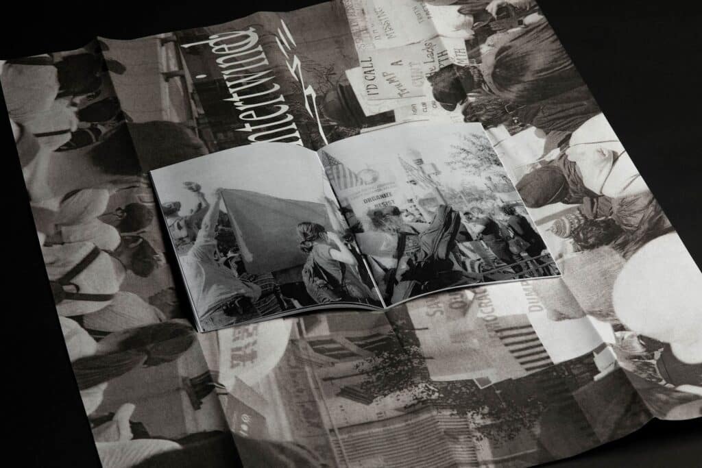 Open zine laid on top of a large folded poster, both featuring black-and-white protest photography with crowds holding banners and signs.