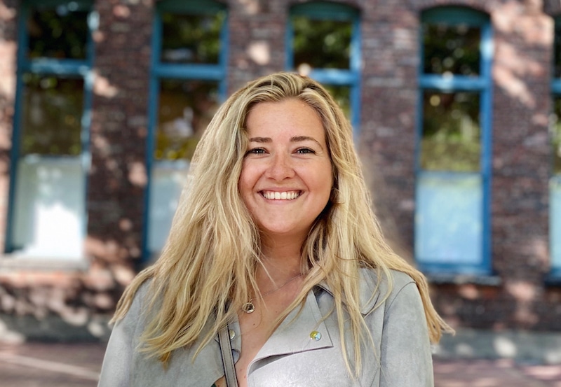 UX Design Certificate alum Jessica Courtney smiles outdoors in front of a brick building with large blue-trimmed windows.