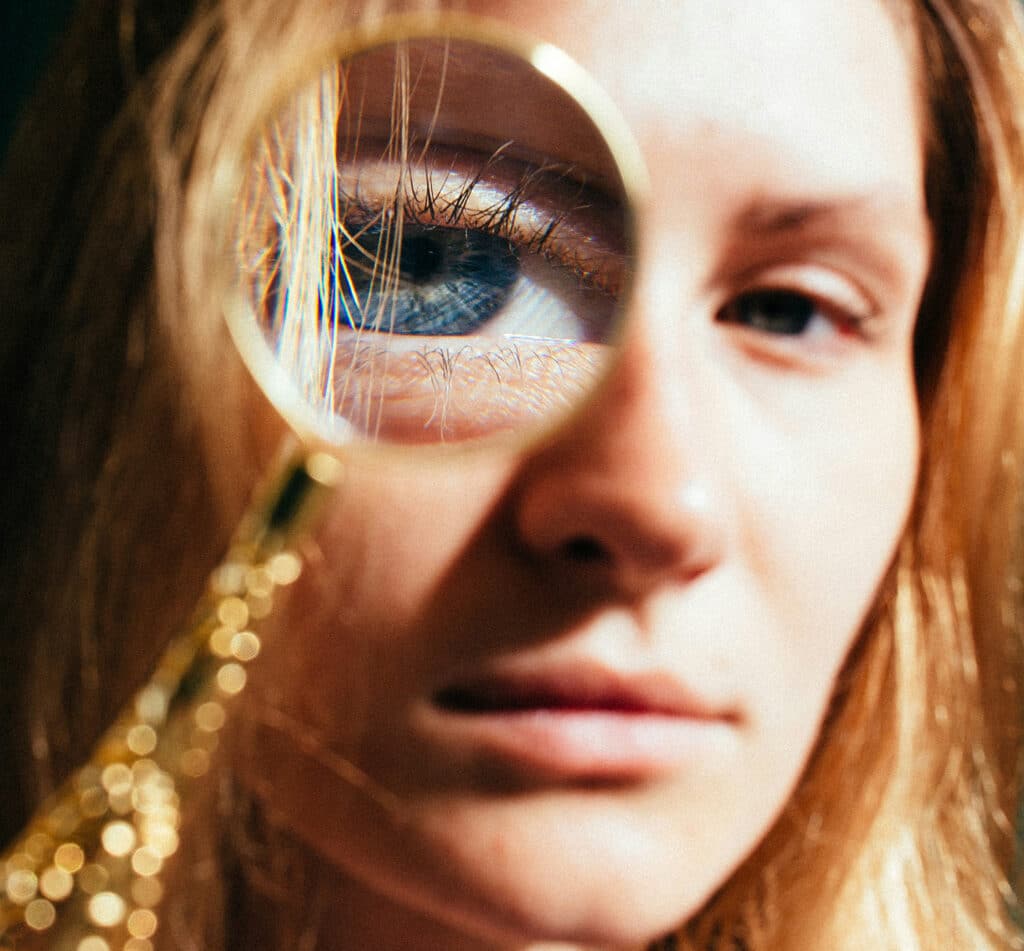 Close-up of a woman holding a magnifying glass over her eye, enlarging her blue iris in sharp detail.