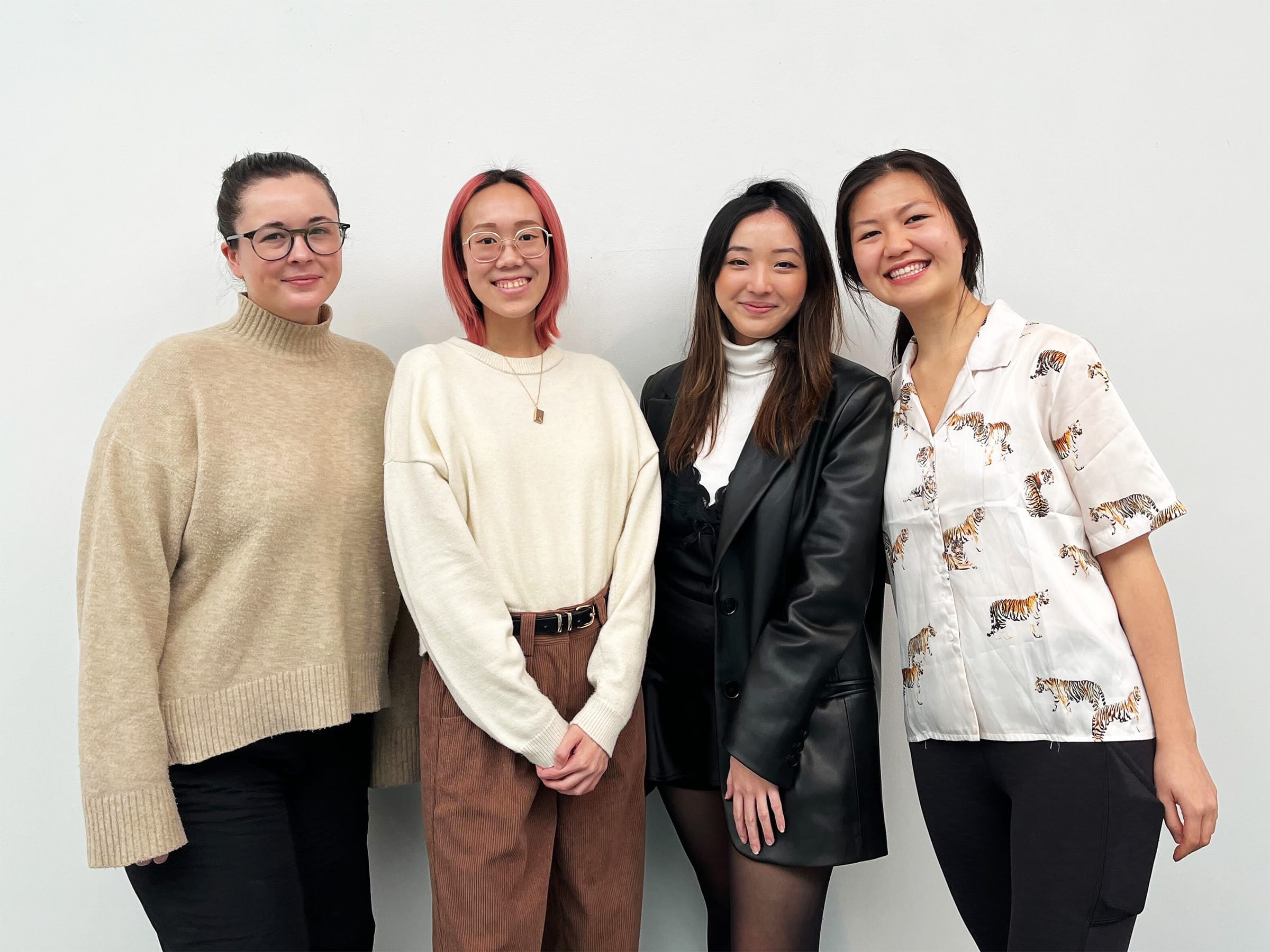 Four UX Design Certificate students — Sydney Batters, Carmen Tin, Diana Tu and Jancis Wong — stand smiling against a white wall. Their team created the award-winning financial literacy app Pygg.