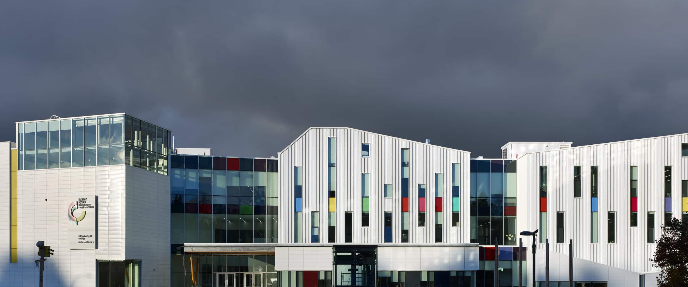 Exterior of Emily Carr University’s Great Northern Way campus under a dark, dramatic sky, with colourful window accents on the white façade.