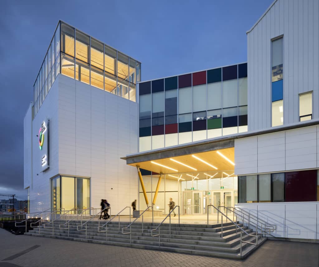 The main entrance of Emily Carr University at dusk, with warm lights glowing inside and students walking past the steps.