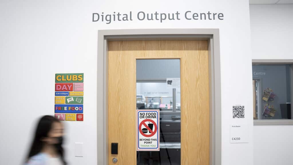 A wooden door with a “No Food or Drink” sign, under the label Digital Output Centre, with a colourful Clubs Day poster on the wall beside it.