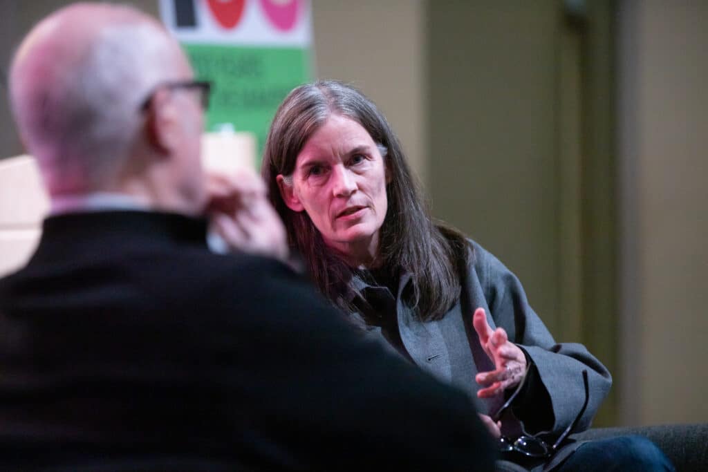 A person speaks during a public conversation on stage at Emily Carr University, gesturing while addressing another person.