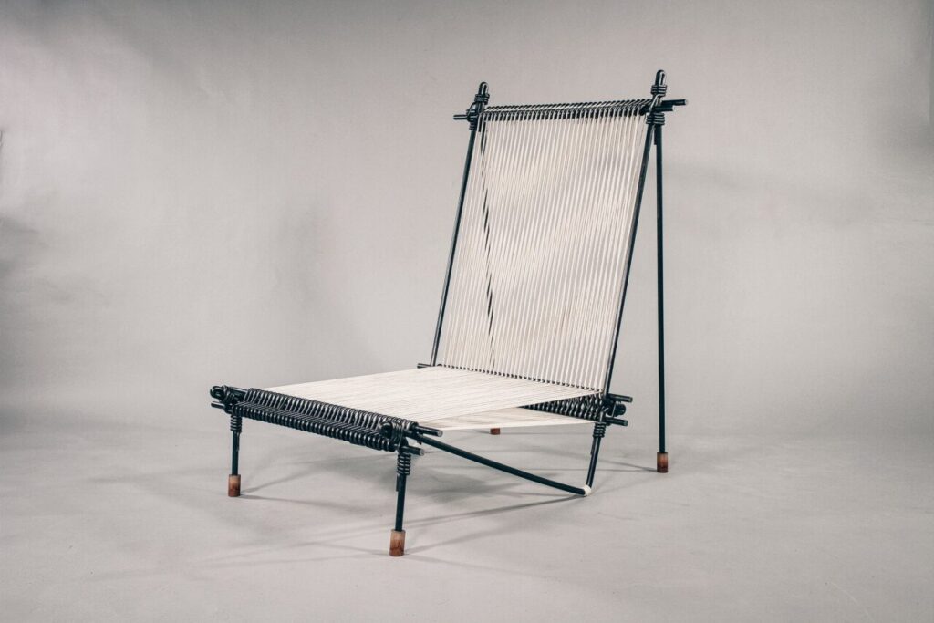 A contemporary chair made of black metal rods and white cord, featuring a minimalist woven seat and backrest, photographed against a plain grey background.