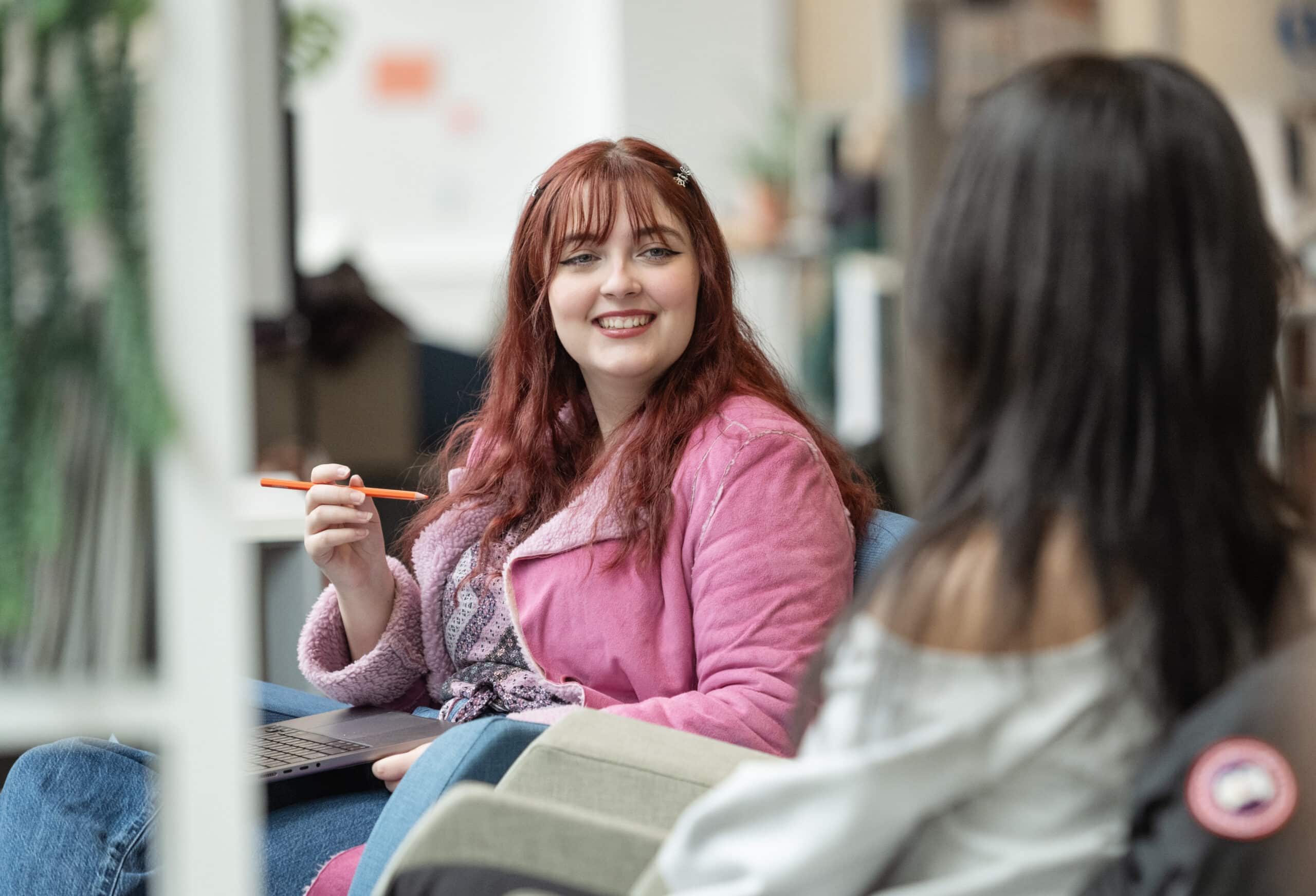 Two students chat and smile in a bright lounge space, creating a welcoming and relaxed atmosphere.