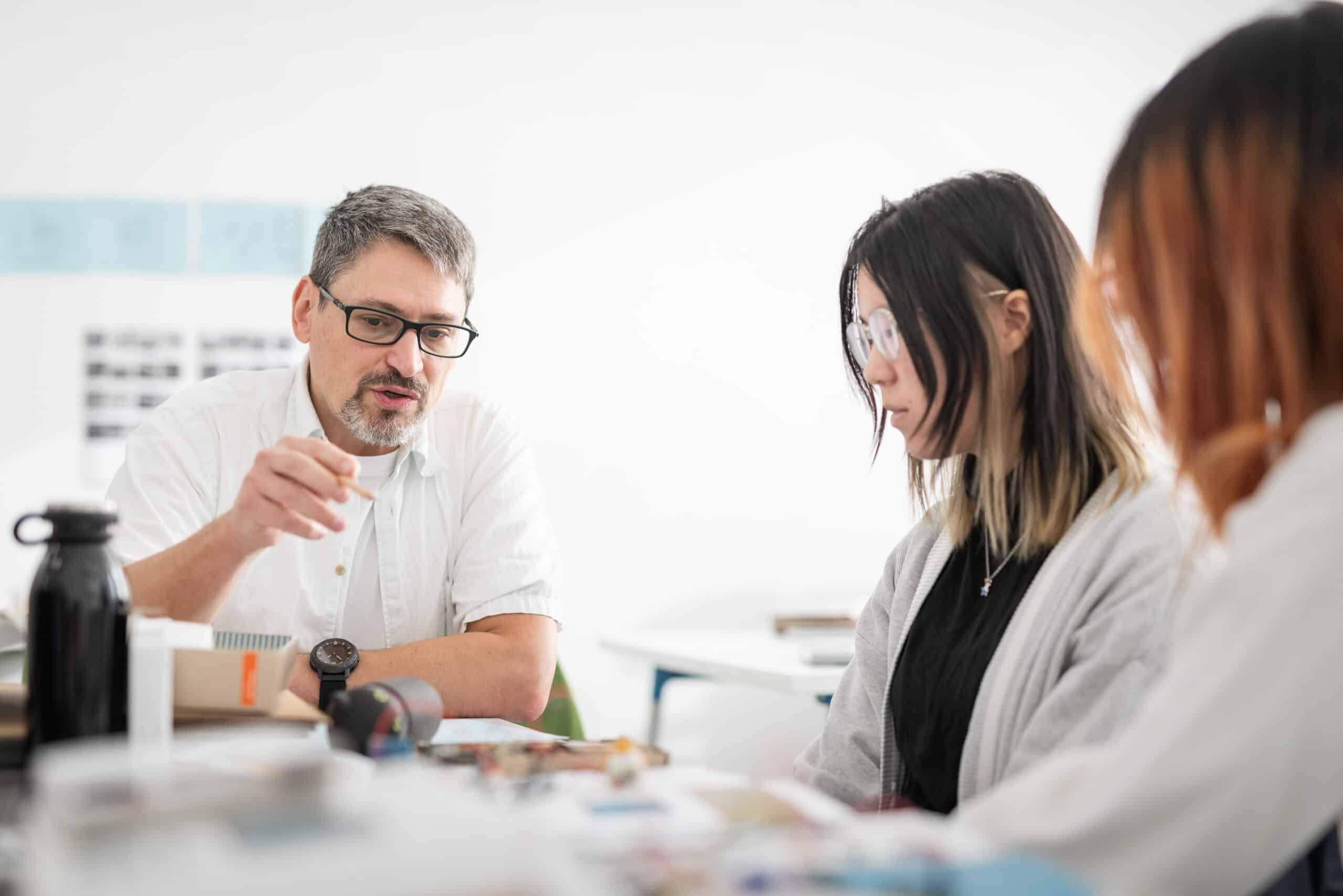 A faculty member meets with two students, offering advice during a classroom discussion.