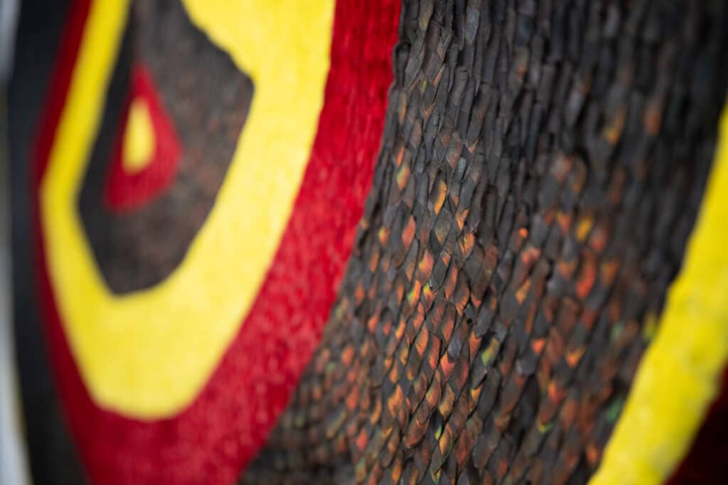 A detailed view of a textile featuring overlapping, scaled pieces in black, red, and yellow forming concentric patterns.