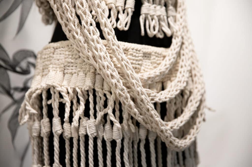 A close-up of a woven textile in cream-coloured fibre with braided and knotted details draped over a mannequin.
