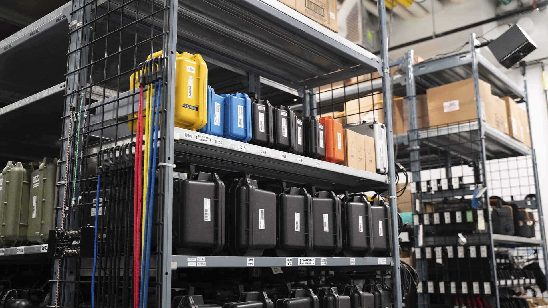 Shelves filled with colour-coded hard cases and equipment, with coiled cables and straps hanging on the side.