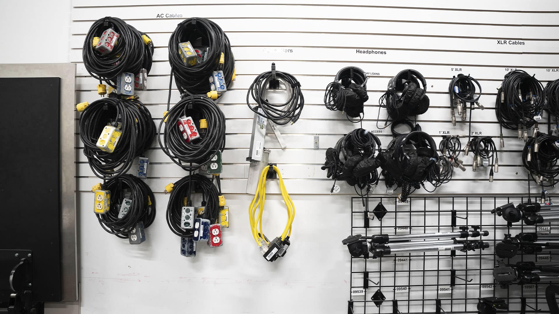 A wall of organized cables and headphones, with AC cables, XLR cables, and tripods neatly hung on hooks.