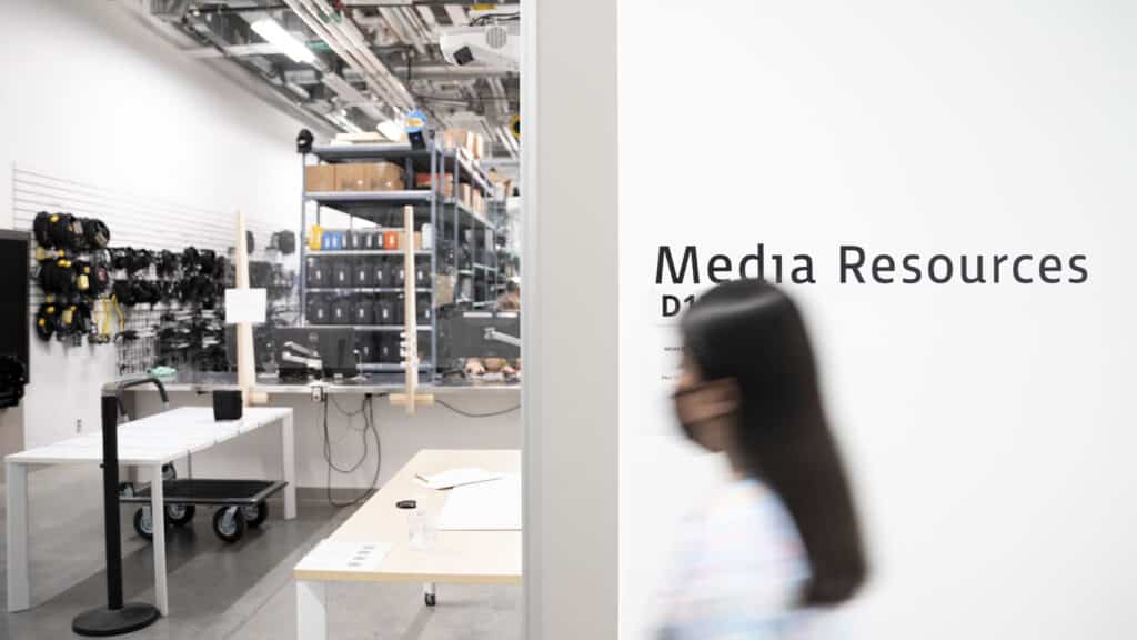 A hallway view into Media Resources, with shelves of equipment visible and a student walking past a sign on the wall.