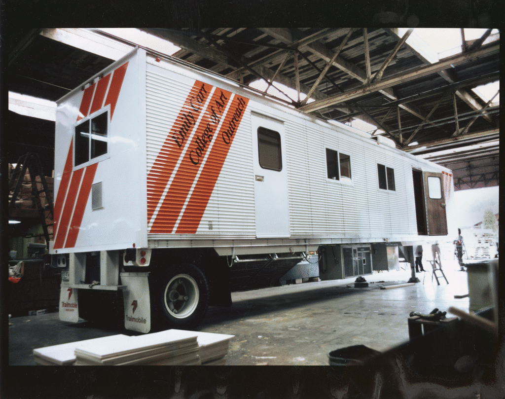 A large trailer marked “Emily Carr College of Art Outreach” parked inside an industrial garage.
