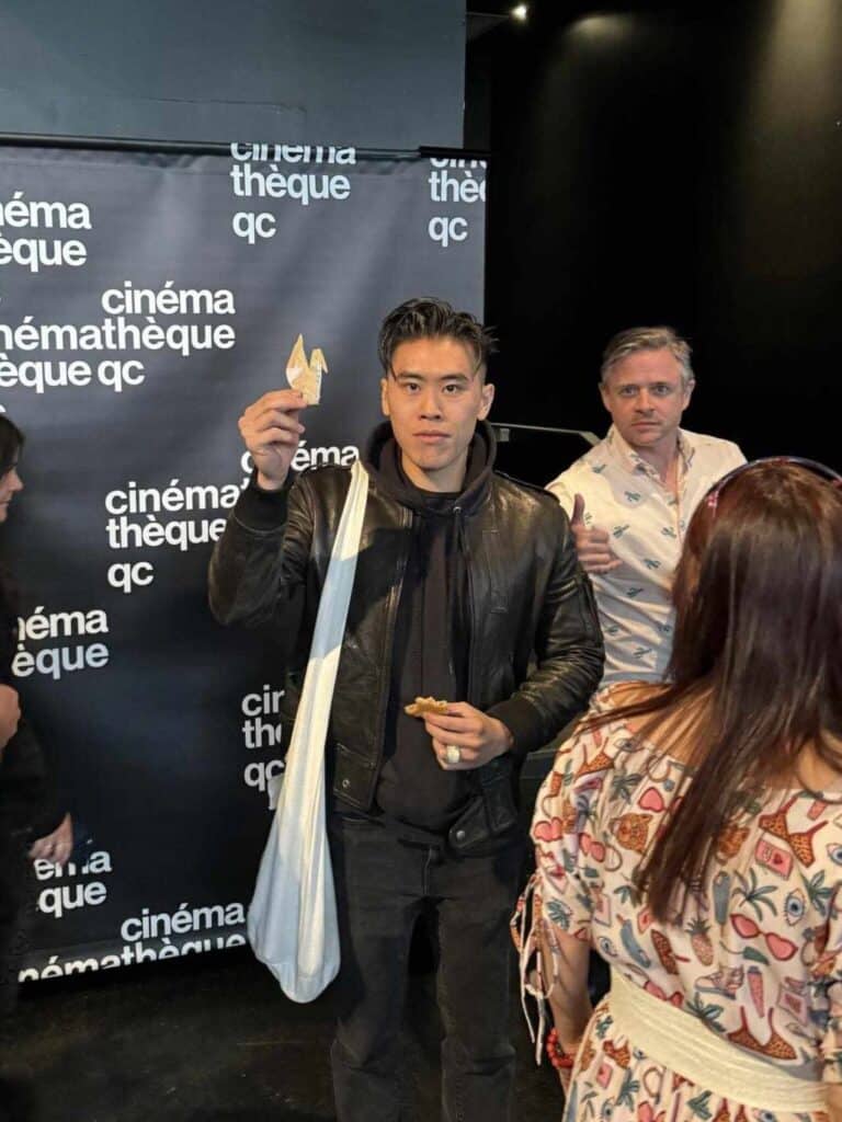 A person holding a small paper object poses for a photo at an event in front of a black backdrop with the Cinémathèque Québécoise logo.