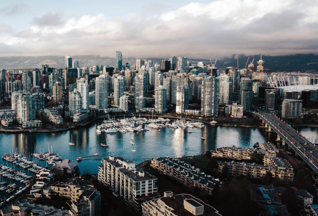 Aerial view of False Creek and downtown Vancouver on a cloudy day, with BC Place Stadium visible in the background.