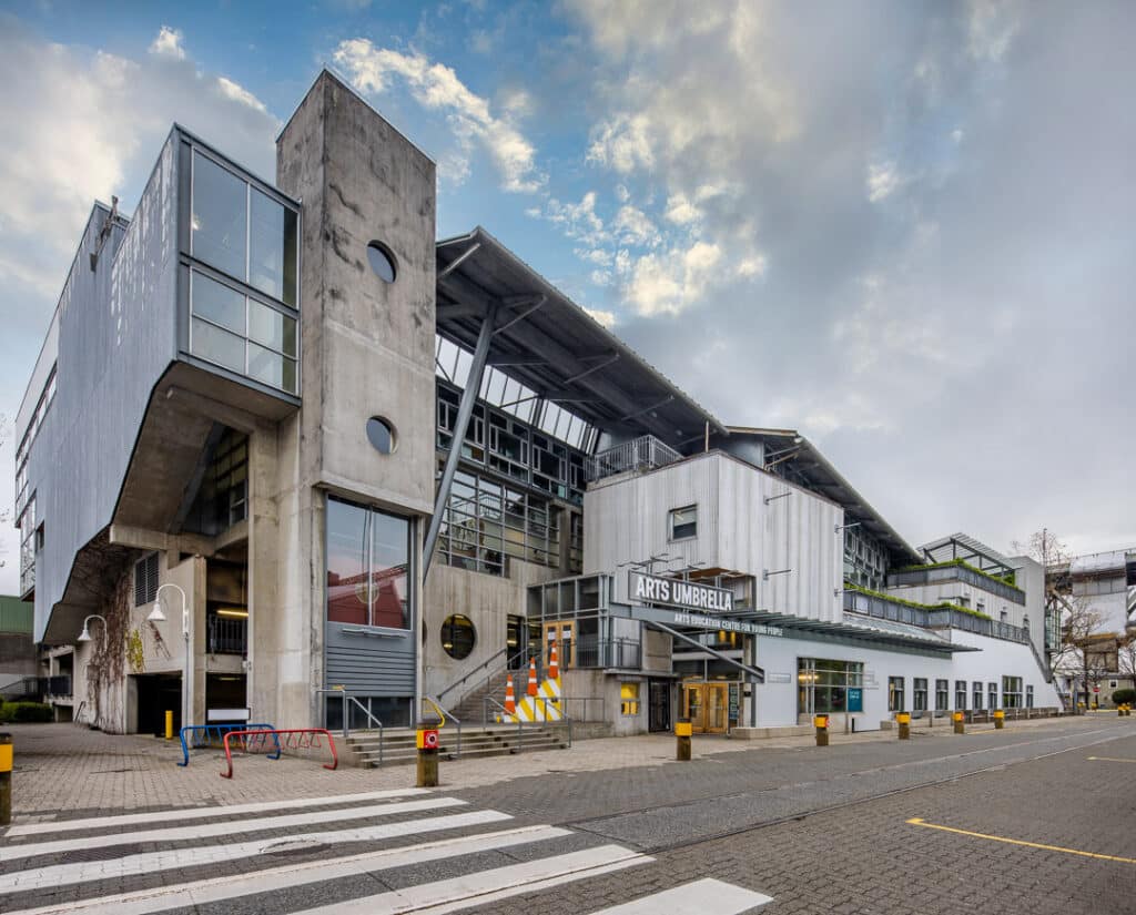 Exterior of the Arts Umbrella building on Granville Island, featuring concrete and glass architecture under a cloudy sky.
