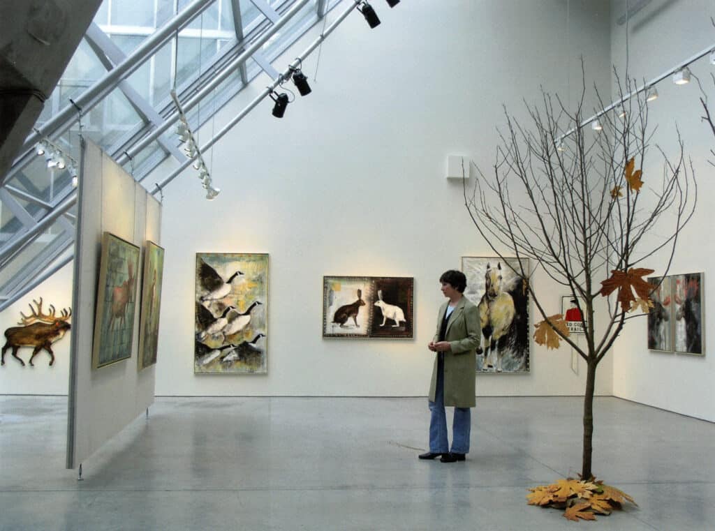 Artist viewing animal-themed paintings in a bright gallery space with angled skylights.