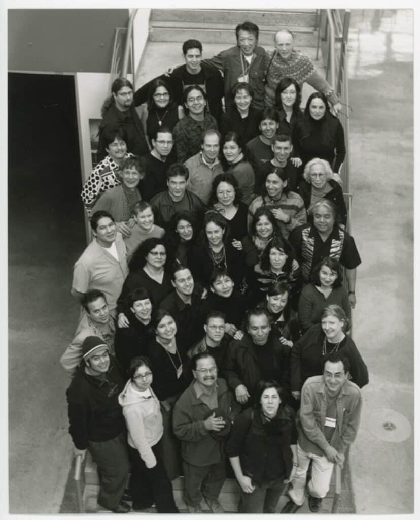 Roughly two dozen people stand on a staircase looking upward in a black-and-white group portrait.