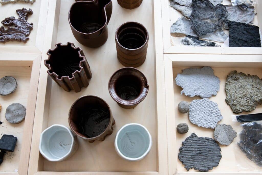 A collection of ceramic vessels and experimental handmade material samples arranged in wooden display trays, showing varied textures, colours and forms.