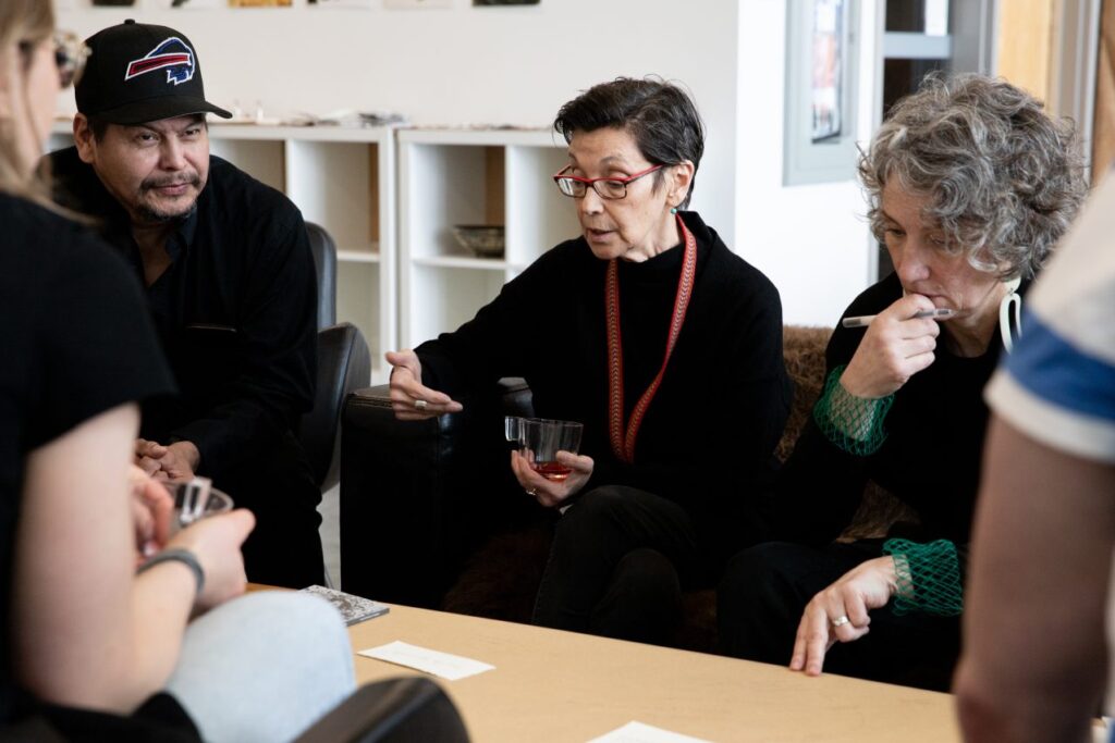 A small group seated in a studio space reviewing prints and textured material samples during a guided discussion.