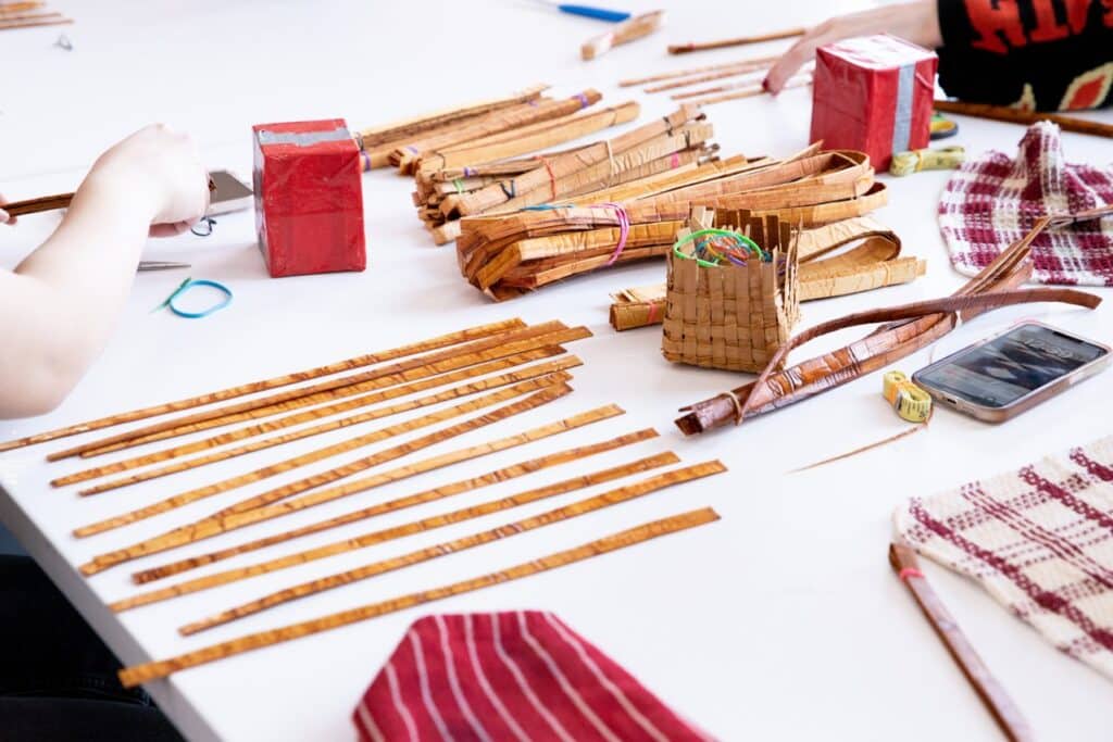 A table is covered in textiles and cedar strips in bundles and laid out flat.