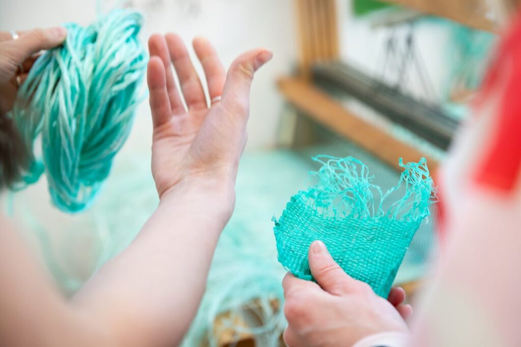 Two pairs of hands hold a series of textiles made of green fibre.
