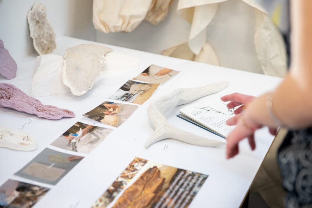A white desk covered photos, notebooks and objects resembling antlers, plants and rocks.
