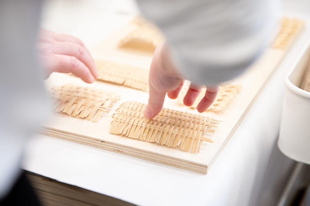 A pair of hands reaches for one among a series of woven wicker patterns.