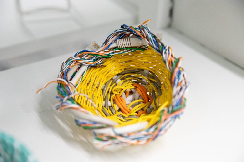 A small basket woven from brightly coloured electrical cables on a white shelf.