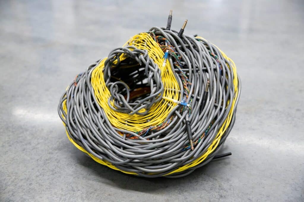 A collapsing basket woven from grey and yellow electrical cables on a concrete floor.
