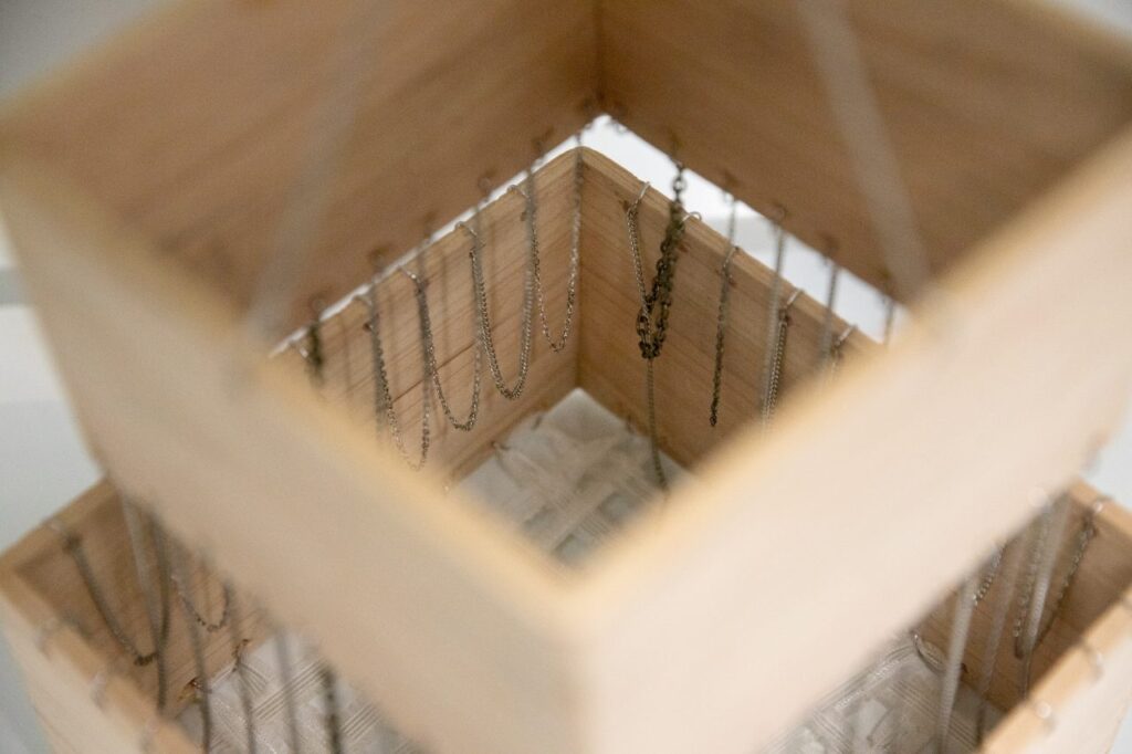 A close-up of a pair of nested cedar boxes connected by delicate silver chains.